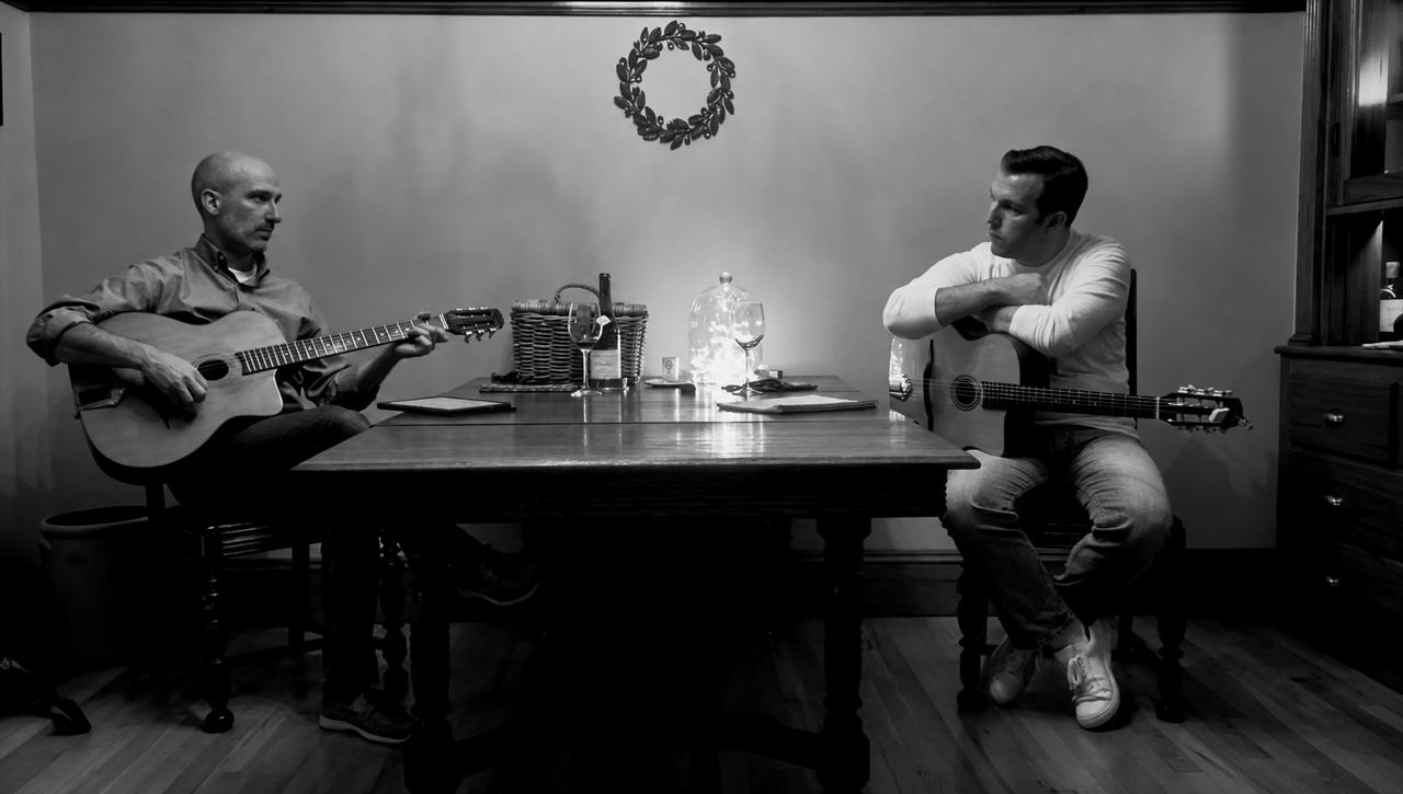 Two guitarists sharing a quiet moment of music at a table
